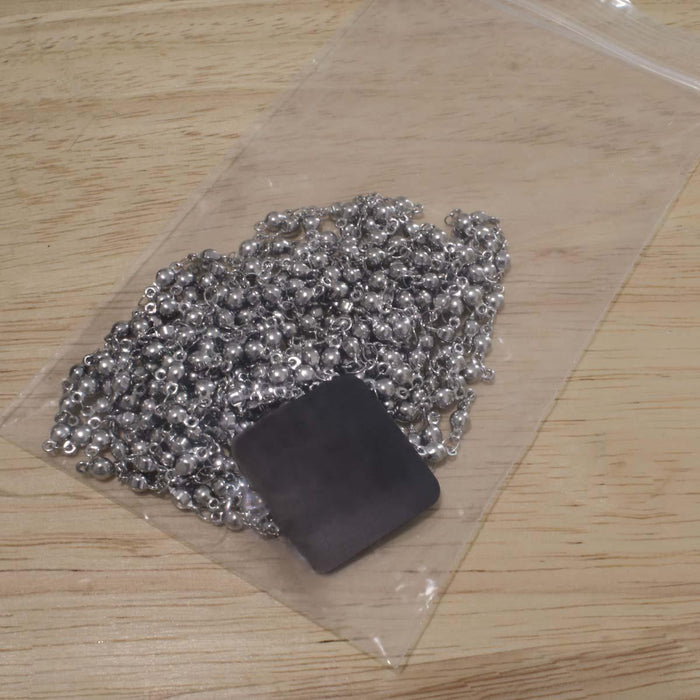 Anti-tarnish tab placed in a clear zip bag with silver chain to prevent tarnish, on a wood surface
