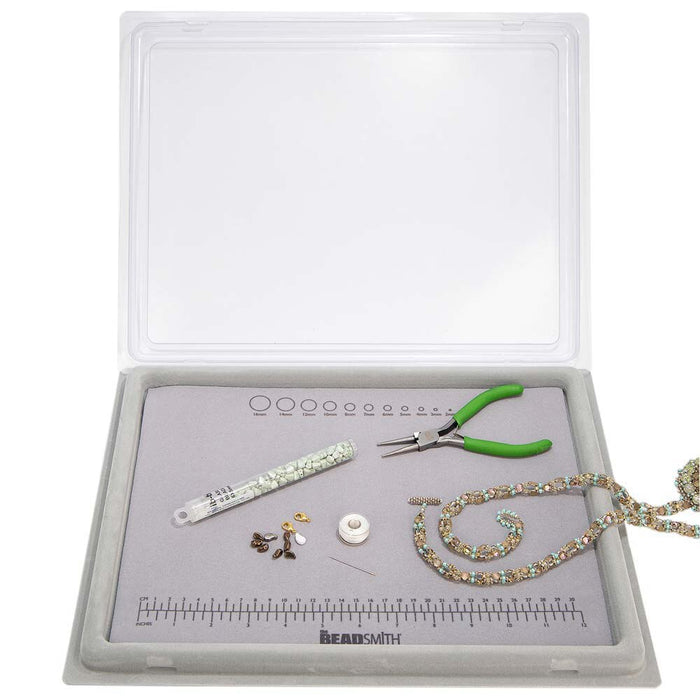 Bead mat tray with clear cover lifted above beading tools, tube of seed beads and a beaded necklace on the mat