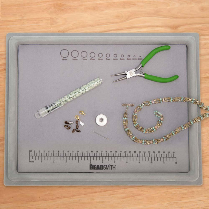 Top view of flocked bead mat tray on a wood table with pliers, beads, findings and beaded necklace on the ruler mat