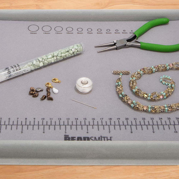 Close-up of flocked bead mat tray with measuring ruler and bead size circles, holding pliers, beads and a beaded strand
