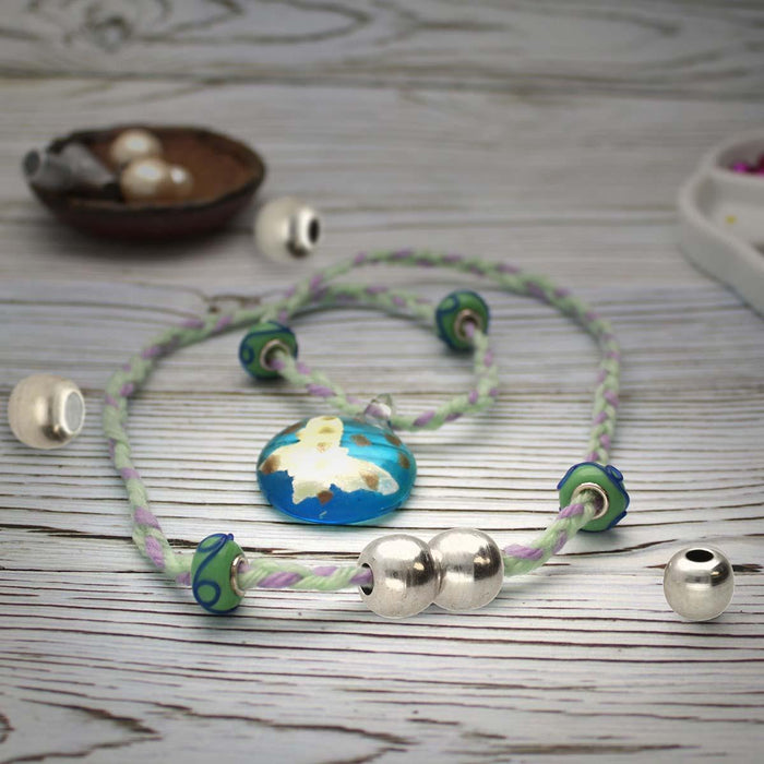 Antiqued silver magnetic ball clasp on a green and lavender braided bracelet with glass beads on a wood surface