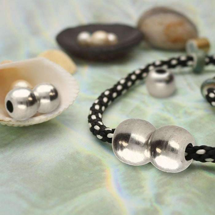 Antiqued silver magnetic ball clasp joined on a black and white braided cord bracelet next to a seashell