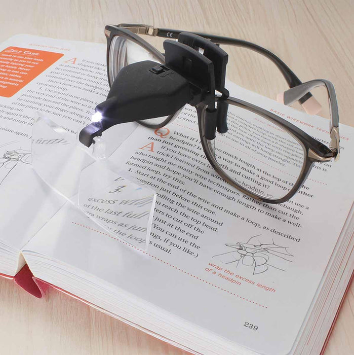 LED magnifier clipped to glasses with light on, magnifying text in an open beading book