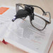 LED magnifier clipped to glasses with light on, magnifying text in an open beading book