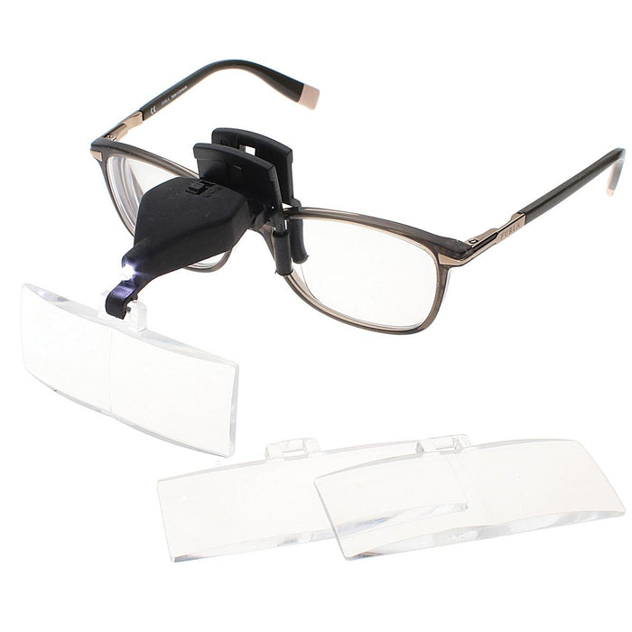 Clip-on LED magnifier attached to eyeglasses with lit light, two spare lenses laid in front
