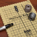 Close-up of the macrame board grid with beads on cord, two cord spools and a threading tool