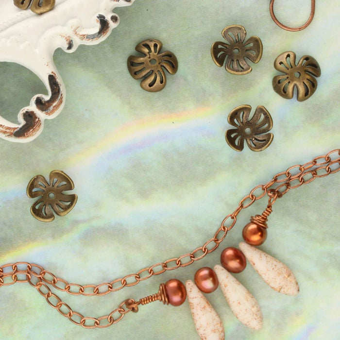 Antiqued brass flower bead caps beside a copper chain necklace with pearls and cream beads on a pastel surface