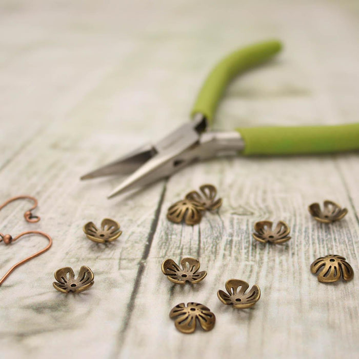 Antiqued brass flower bead caps on a wood surface with green-handled pliers and copper ear wires