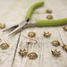 Antiqued brass flower bead caps on weathered wood beside green-handled pliers and a copper ear wire