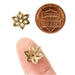Antiqued brass flower bead caps beside a US penny and resting on a fingertip for scale