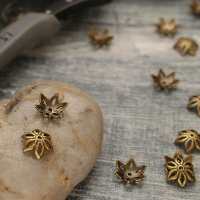 Close-up of antiqued brass flower bead caps on a smooth stone and gray wood surface