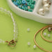 Crystal bead necklace with toggle clasp, loose beads and coiled gold wire on a green background for jewelry making