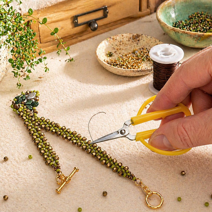 Hand using the mini scissors to trim thread on a beaded bracelet at a beading workspace