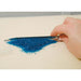 Hand using the Scoop-EEZ bead scoop to gather a pile of tiny blue seed beads from a flat surface