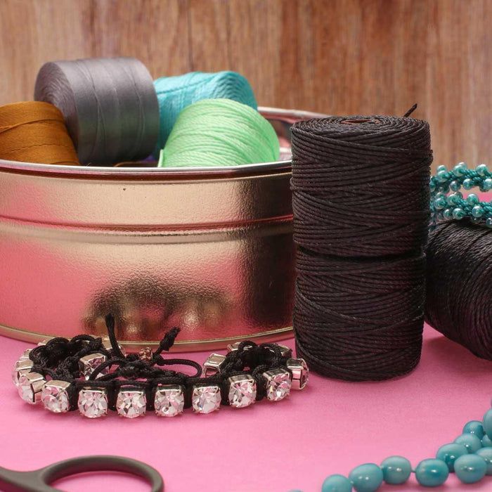 Black S-Lon nylon cord spools beside a rhinestone bracelet, turquoise beads and other colored spools in a tin