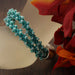 Teal beaded macrame bracelet made with S-Lon nylon cord and seed beads, displayed near orange flowers