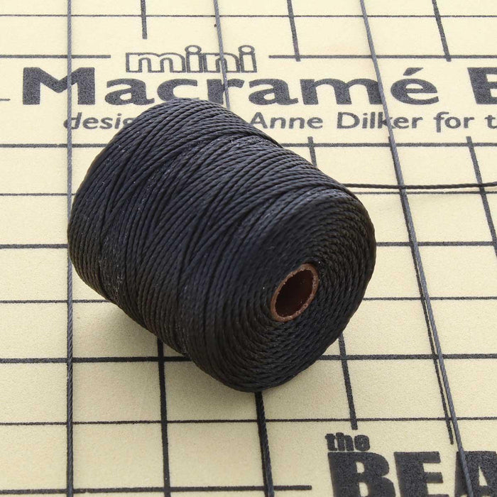 Black S-Lon nylon bead cord spool resting on a mini macramé board with a loose cord end