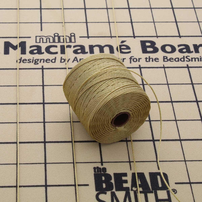Bronze S-Lon bead cord spool with loose cord strands lying on a mini macramé board with grid