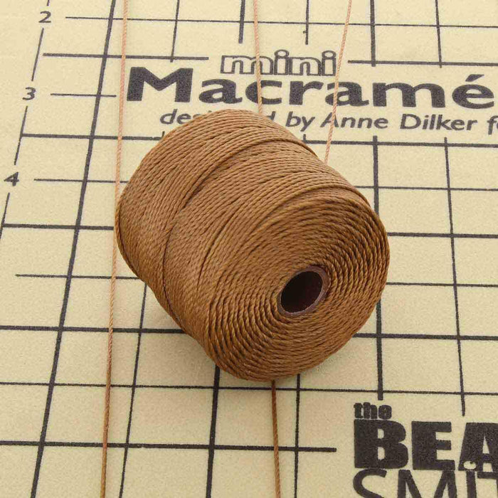 S-Lon milk chocolate nylon cord spool with loose cord strands on a mini macramé board with measurement markings