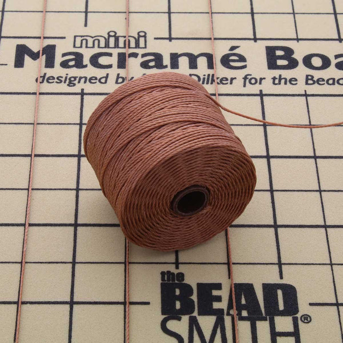 Copper nylon bead cord spool on a mini macramé board with cord strands stretched across it