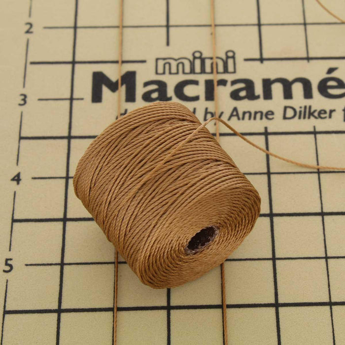 Dark tan S-Lon nylon bead cord spool on a mini macrame board with measurement grid for scale
