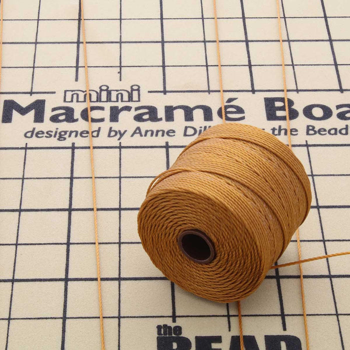 Gold S-Lon nylon bead cord spool with loose cords on a mini macramé board
