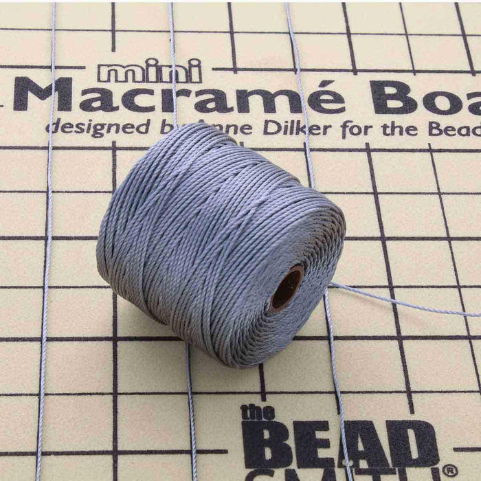 Grey S-Lon nylon bead cord spool resting on a mini macramé board with cord strands laid out