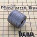 Grey S-Lon nylon bead cord spool resting on a mini macramé board with cord strands laid out