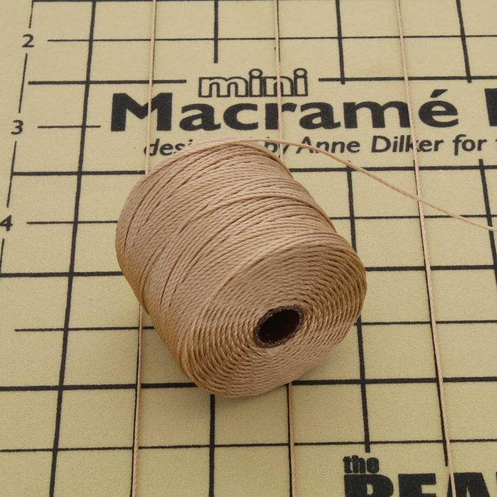 Light brown S-Lon nylon bead cord spool lying on a mini macramé board with measurement grid