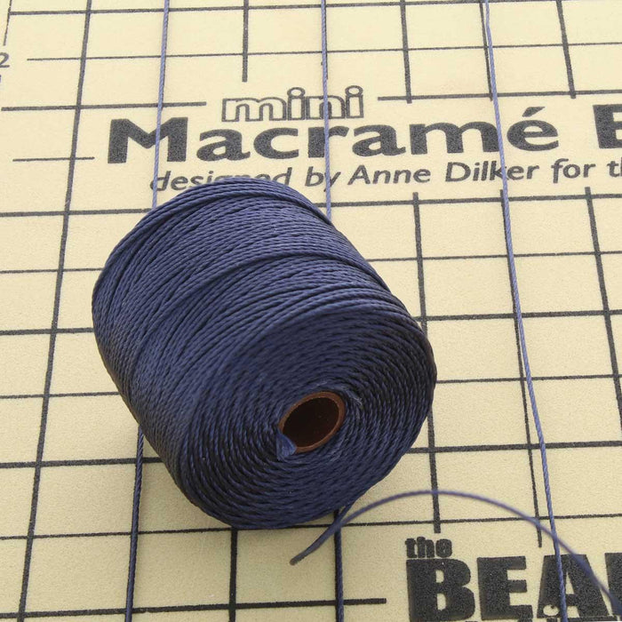 Navy blue nylon bead cord spool with loose end resting on a mini macramé board with grid