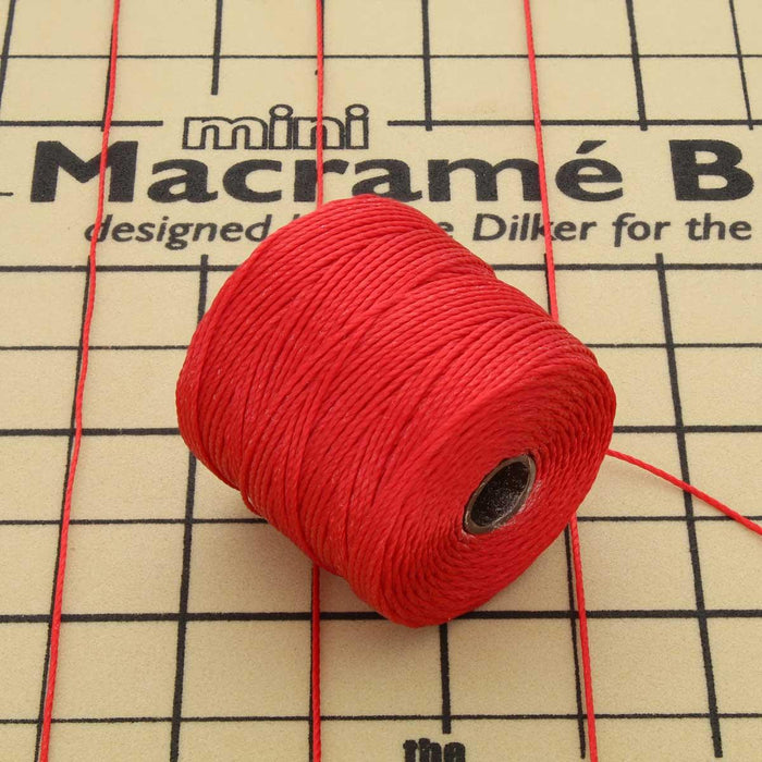 Red S-Lon nylon bead cord spool resting on a mini macramé board with cords stretched across it