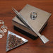 Tweezers with shovel resting on a steel bench block beside a ring, seed bead tray and wire jewelry