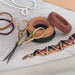 Tan waxed linen cord coil styled with black and brown cord, gold scissors and a knotted beaded bracelet