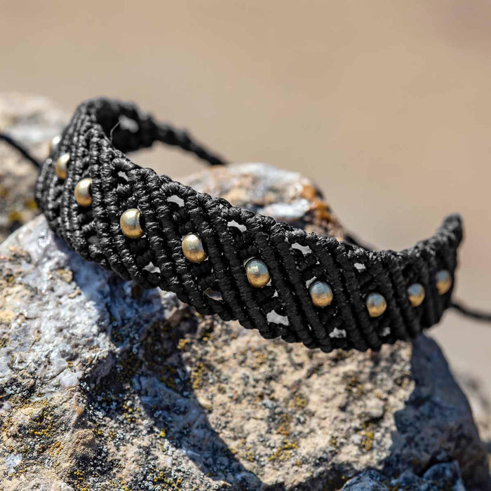 Black knotted macrame bracelet with gold beads resting on a rock, an example of waxed cord jewelry